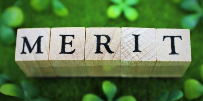 緑の背景に置かれた「MERIT」と書かれた木のブロックとクローバーの葉