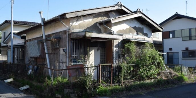 草木に囲まれた老朽化した住宅の外観