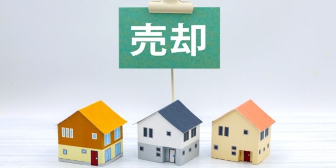 「売却」の札と並ぶ3軒の住宅模型の写真。