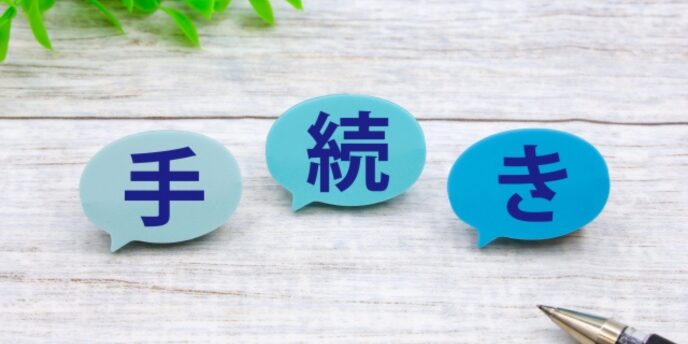 「手・続・き」と書かれた吹き出しが横並びに並んでおり、背景は木目調、右下にペンがある