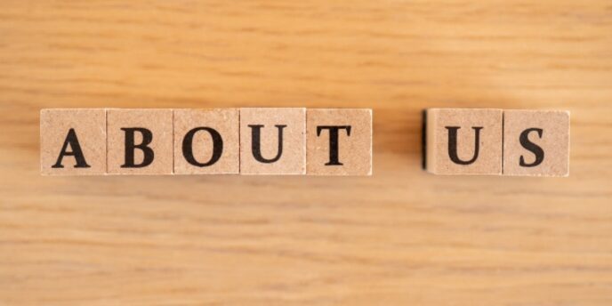 木目の背景に「ABOUT US」と書かれた英字ブロックが並んでいる画像