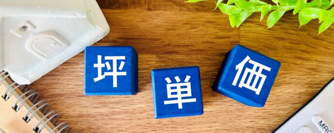 ノート上の青い立方体に配置された「坪単価」の文字とデスク周り