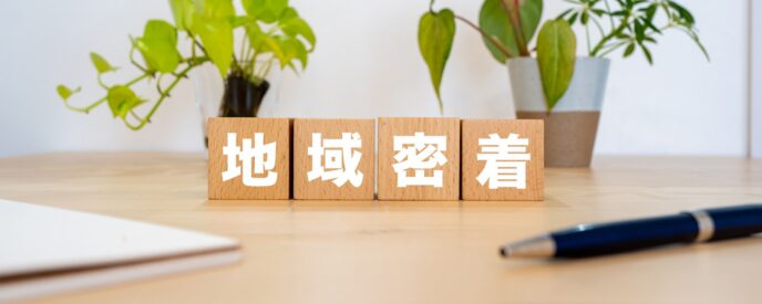 「地域密着」と書かれた木製ブロックと観葉植物