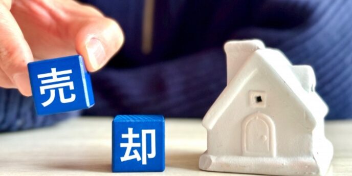家の模型と青いブロックに「売却」と書かれた不動産売却を表すビジュアル