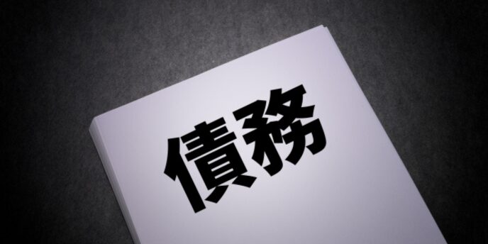 黒背景に置かれた「債務」と書かれた書類のイメージ