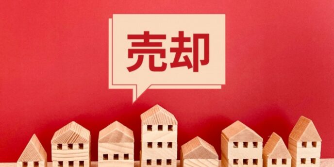 赤い背景と木製の家の模型、吹き出しに「売却」と表示された不動産イメージ