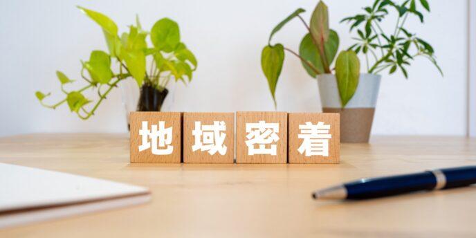 「地域密着」と書かれた木製ブロックが観葉植物の前に並ぶイメージ
