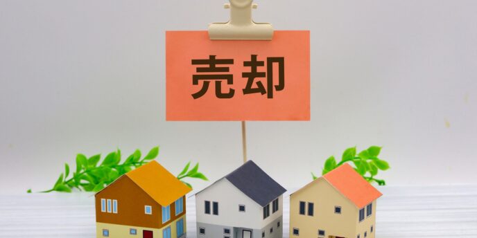「売却」札と住宅模型３棟で不動産売却を表すイメージ