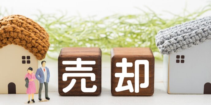 「売却」と書かれた木製キューブと家のミニチュア