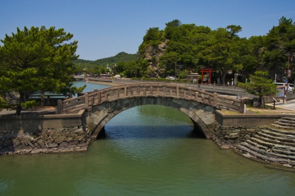 水面に架かる石橋と神社の鳥居がある風景