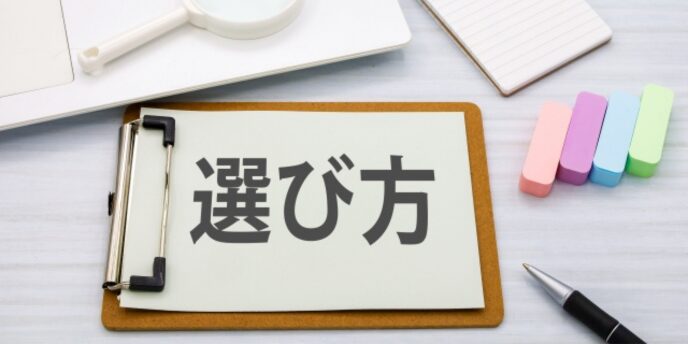 「選び方」の文字が書かれたメモとクリップボード、カラフルな文具のイメージ