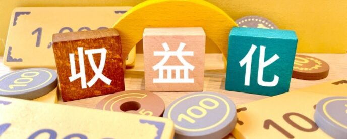 「収益化」の積み木と100の数字トークンが並ぶ収益イメージの写真
