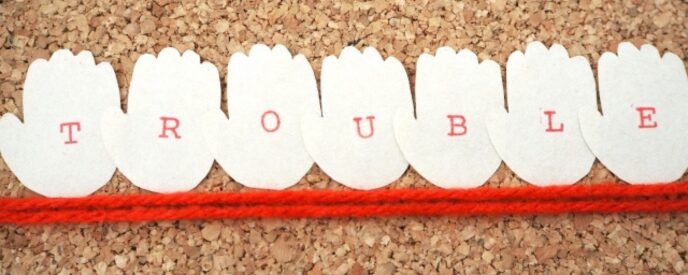 「TROUBLE」と書かれた手の形のカードと赤い境界線のような糸のイメージ
