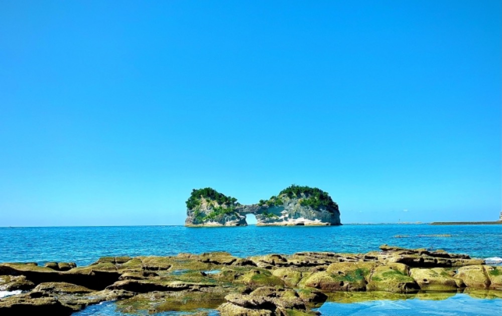 青い海に浮かぶ穴の開いた岩と晴れ渡る空